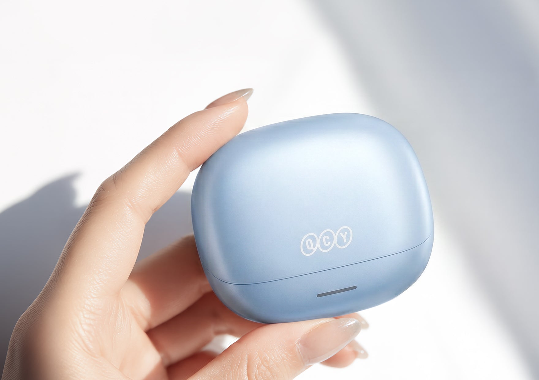Słuchawki Bluetooth QCY w jasnoniebieskim kolorze, trzymane w etui ładującym.