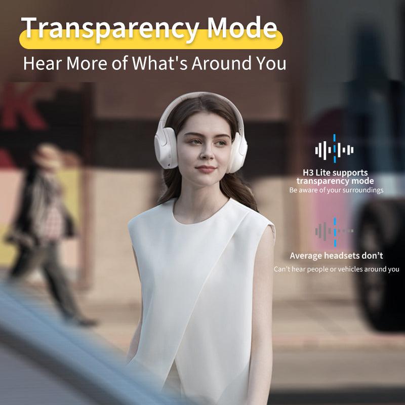 White QCY H3 Lite headphones with transparency mode, allowing awareness of surroundings, shown on model in urban setting.